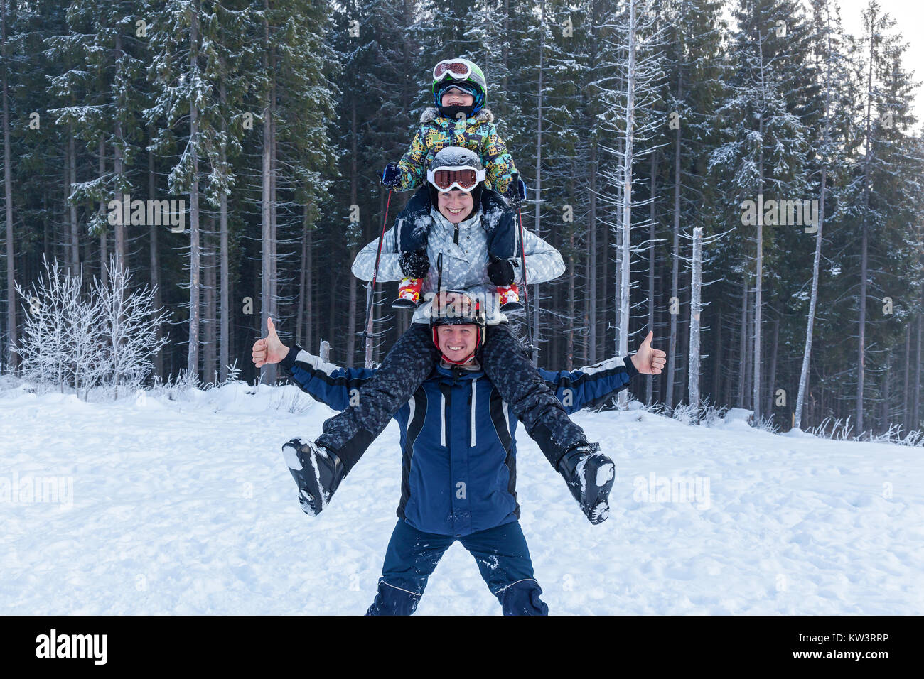 Pyramide Vater Mutter und Kind in Skianzüge auf Urlaub. Junge Mann seine Freundin hält auf seinen Schultern. Mädchen umarmt Kerl für den Hals. Stockfoto
