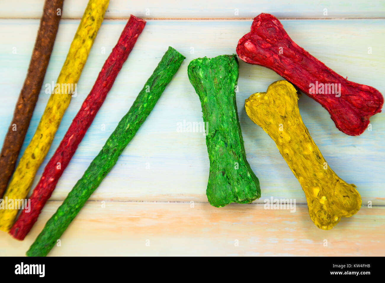 Heimtiernahrung. Bunte chrunchy Snacks in Form von Knochen und Sticks für Hunde auf einem farbigen Hintergrund aus Holz. Platz für Ihren Text oder Bild. Stockfoto