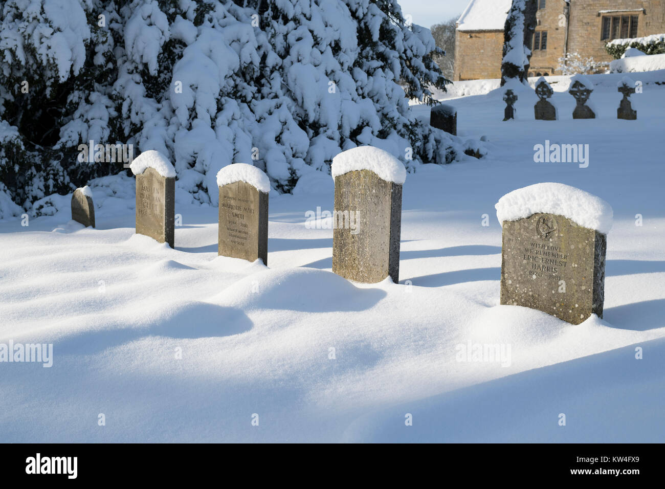 Schnee bedeckt Grabsteine in St. Bartholomä Kirchhof im Dezember Schnee. Notgrove, Cotswolds, Gloucestershire, England Stockfoto