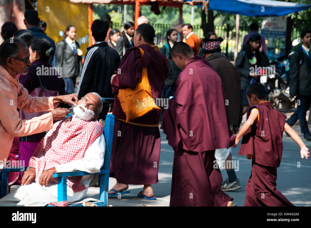 Indien. Bihar. Bodhgaya. Friseur bei der Arbeit auf der Strasse ... Rasieren ein Kunde während einer Gruppe von Mönchen Spaziergänge durch. Stockfoto
