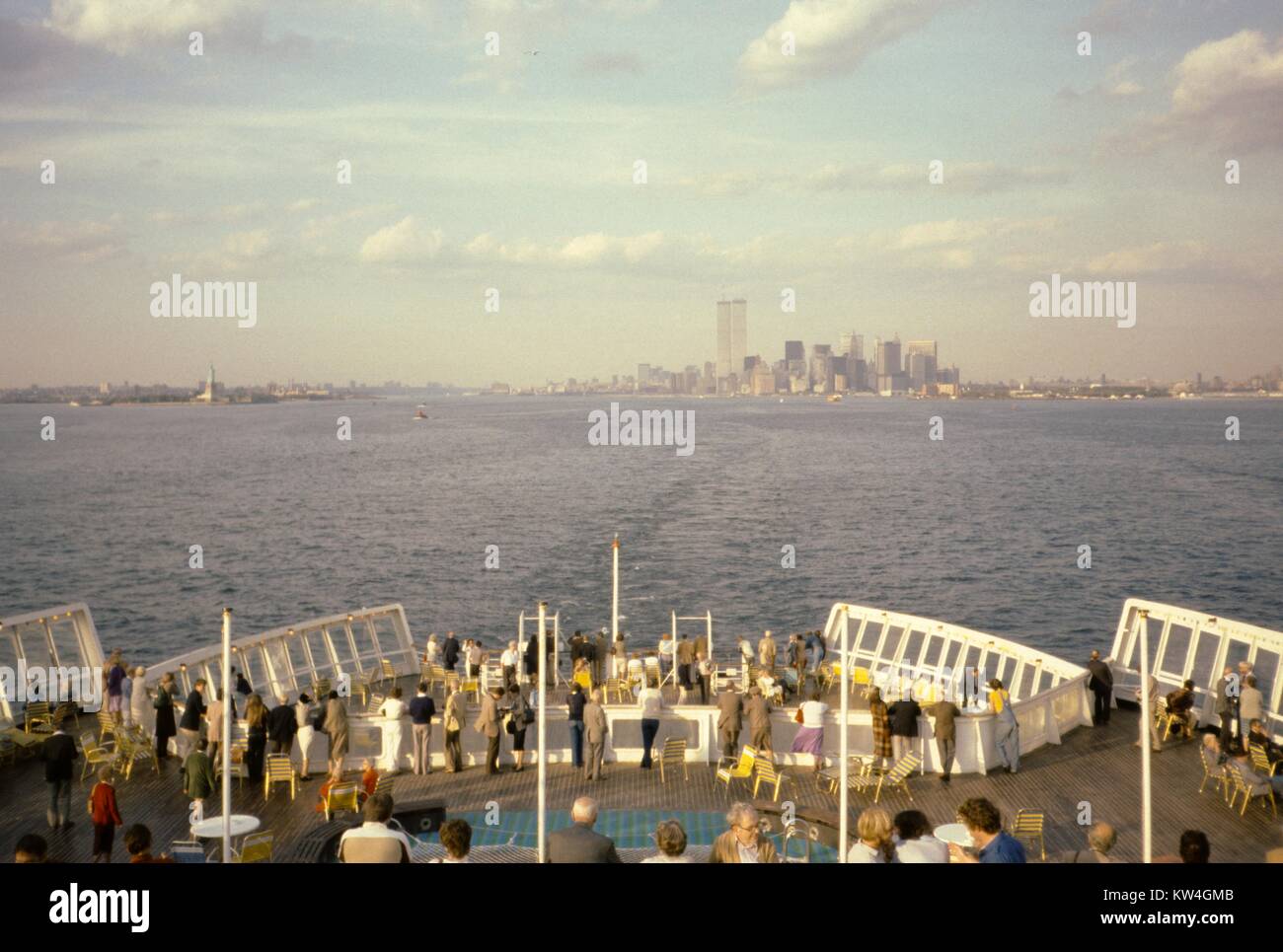 Skyline von New York City, darunter das Twin Touren des World Trade Center, und die Freiheitsstatue, die von einer Gruppe von Touristen auf dem Achterdeck der Queen Elizabeth 2 Kreuzfahrtschiff der Cunard Line versammelt gesehen, am Meer, New York, 1975. Stockfoto