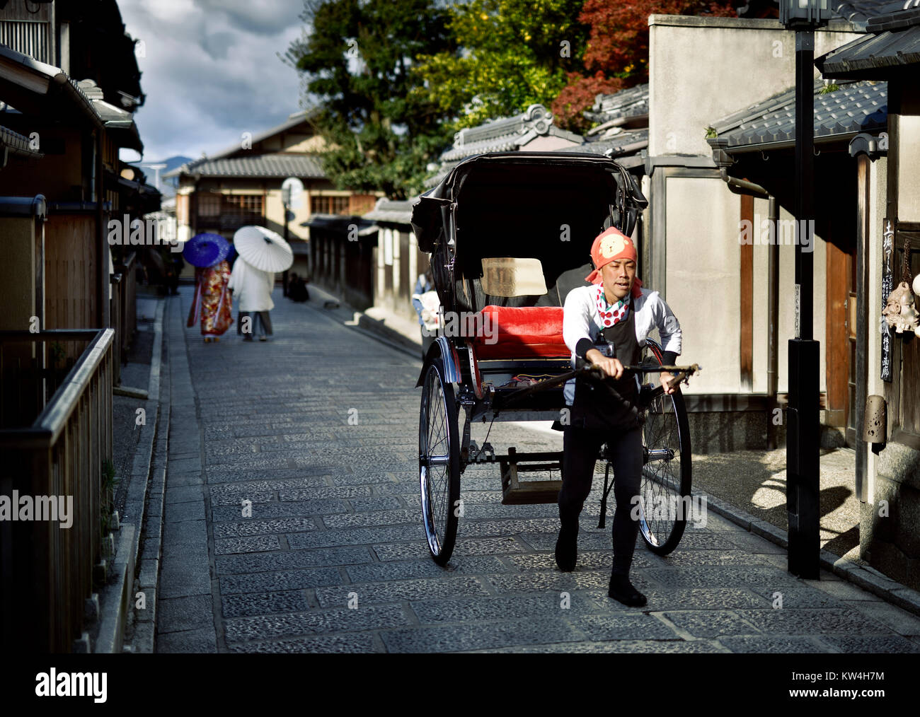 Führerschein und Fingerabdrücke bei MaximImages.com - japanische Rikscha in einer alten Straße in Kyoto mit einem Paar, das Kimonos im Hintergrund trägt. Yasaka Dori, in der Nähe Stockfoto