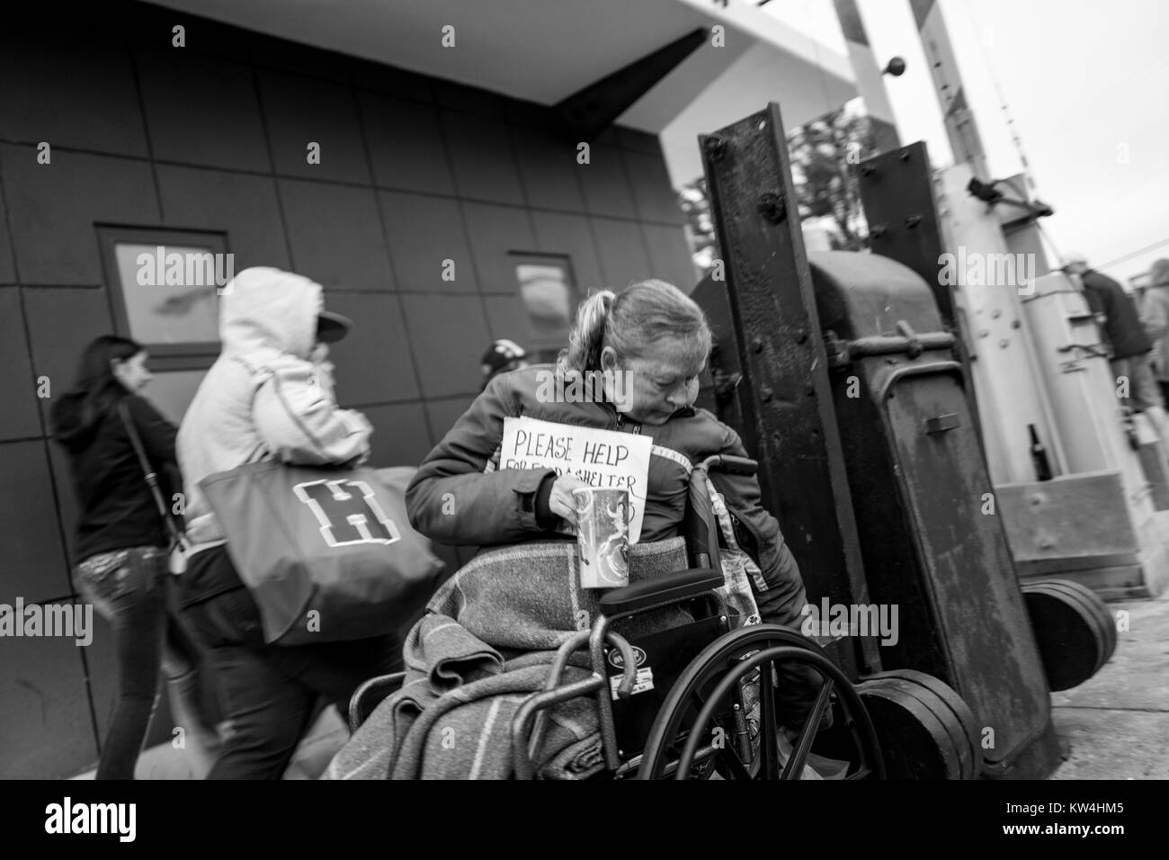 China Becken in der Nähe von San Francisco, Kalifornien, eine obdachlose Frau in einem Rollstuhl hält ein Schild um Hilfe zu bitten, während zwei junge Frauen schnell Vergangenheit, San Francisco, Kalifornien, 21. August 2016. Stockfoto
