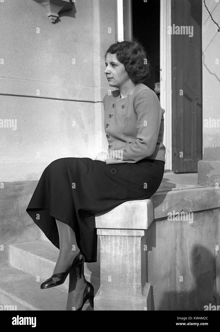Portrait einer hübschen jungen Frau trägt eine geknöpfte Bluse, langer Rock, Strumpfhosen und Heels, sitzt auf der Kante einer Beton Treppe im Freien und sie starrte - Kamera, Ungarn, 1929. Von einem Gelatine Prozess Glasplatte negative digitalisiert. Stockfoto