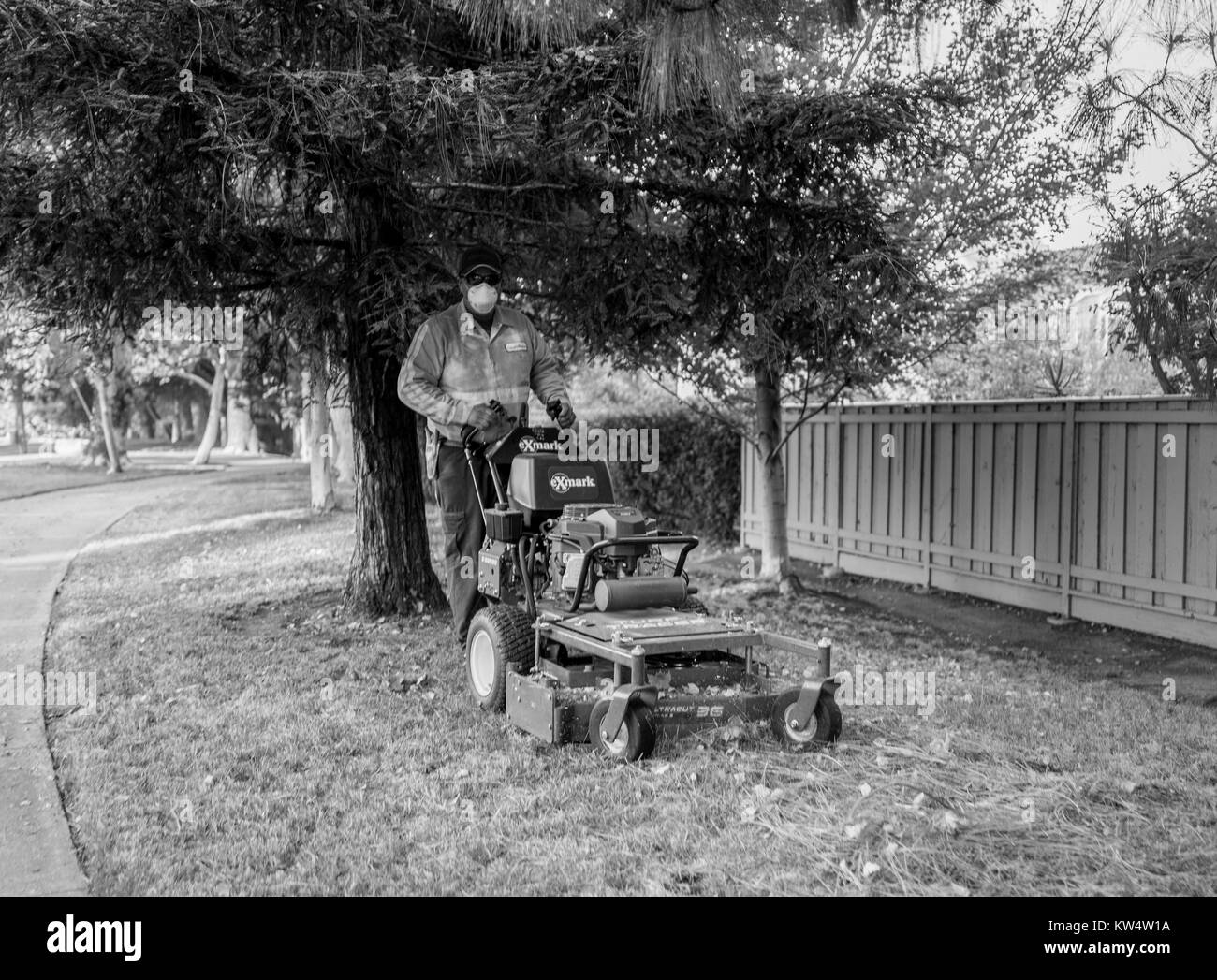 Schwarz-weiß-Bild von einem Landschaftsgestalter das Tragen einer Staubmaske und steht mit seinem stoßmäher entlang einer Straße in Walnut Creek, Kalifornien, 14. September 2016. Stockfoto