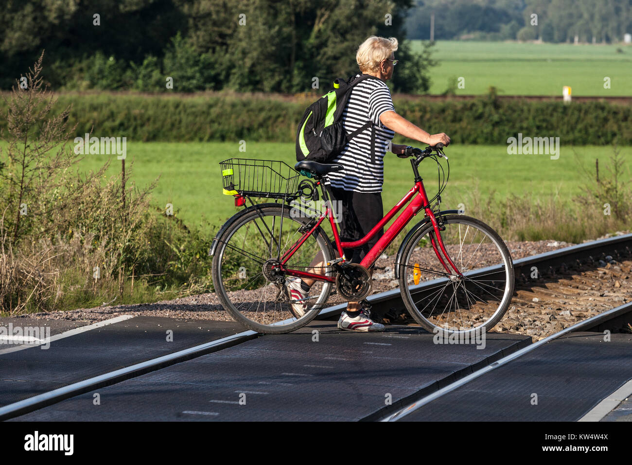 Eine ältere Frau mit Fahrrad überquert die Gleise an einem Bahnübergang, ein Radfahrer allein, eine Frau, die Fahrrad schiebt Stockfoto