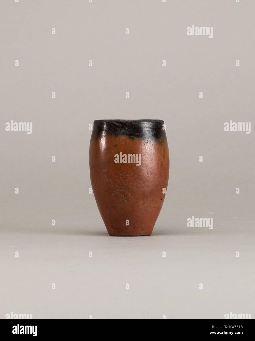 Dieses rote Gefäß mit schwarzem Verschluss, katalogisiert als MET 66.99.192, ist ein bemerkenswertes Beispiel für antike keramische Handwerkskunst, das sich in der Sammlung des Metropolitan Museum of Art befindet Das Glas hat ein markantes Design mit einem kontrastierenden schwarzen Oberteil und einem roten Körper, was die Geschicklichkeit des Töpfers beim Formen und Dekorieren von Töpferwaren unterstreicht. Stockfoto