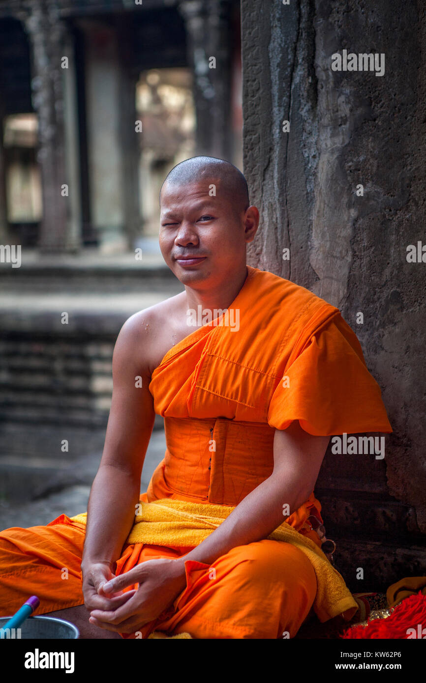 Buddhistischer Mönch mit einem Sinn für Humor zwinkert der Fotograf innerhalb der alten Tempelanlage von Angkor Wat, Siem Reap, Kambodscha sitzen. Stockfoto