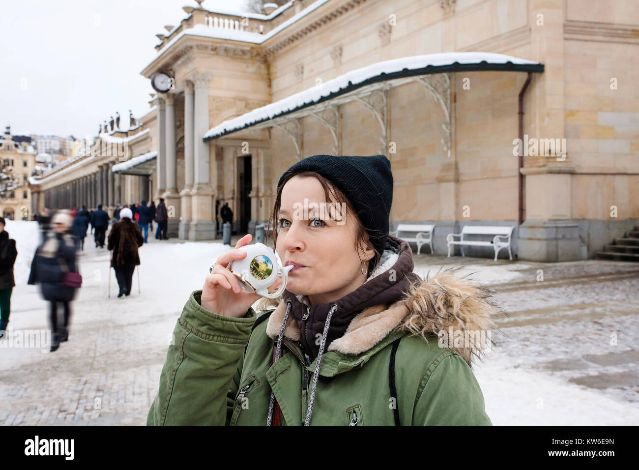 Junge Frau trinkt von Tasse mit therapeutischen Mineralwasser bei einer natürlichen heißen Quelle in Karlsbad im Winter, Tschechische Republik Stockfoto