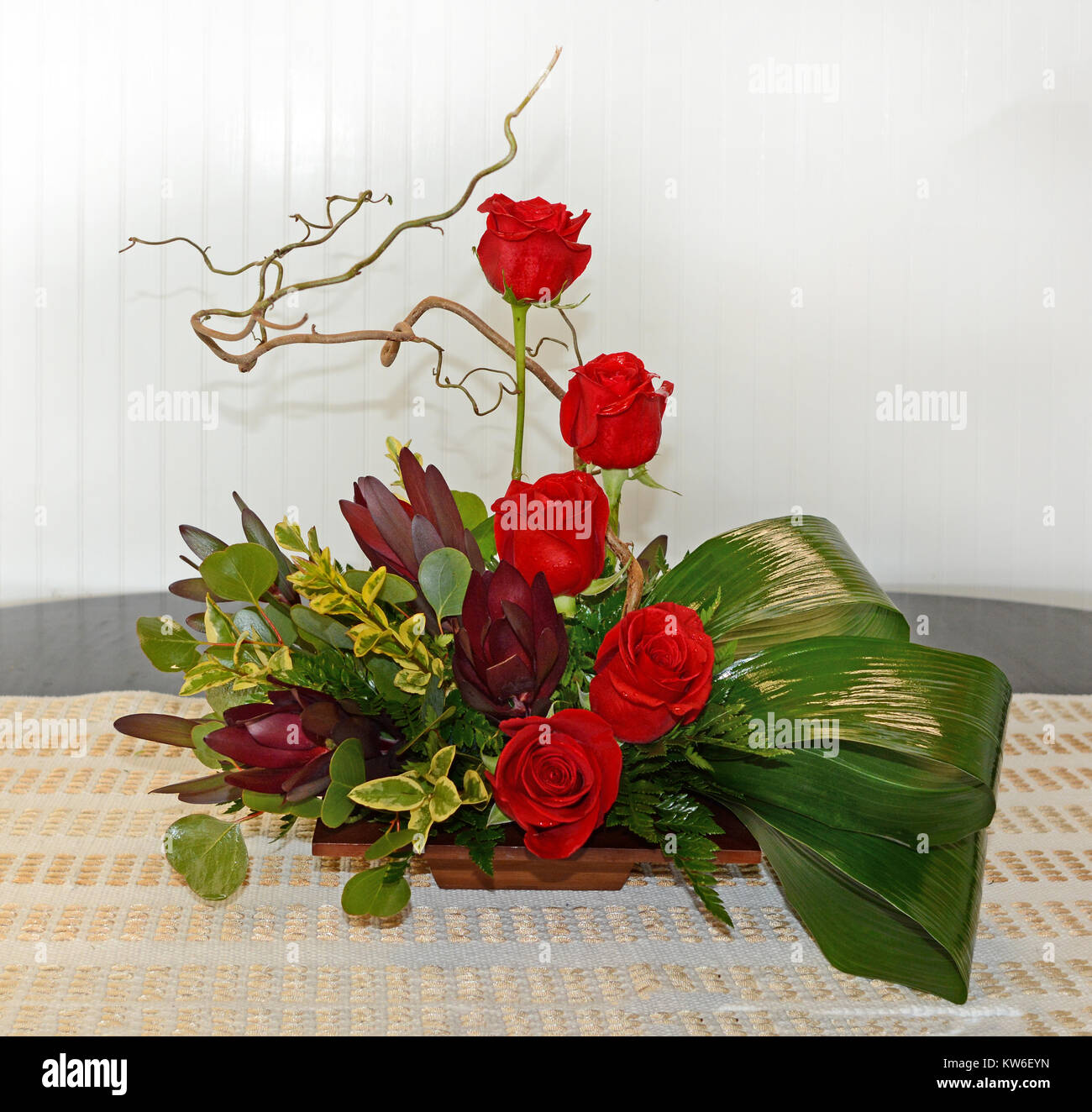 Ein hoher Stil Herzstück bietet Leucadendron, rote Rosen, Zweige und Laub. Stockfoto