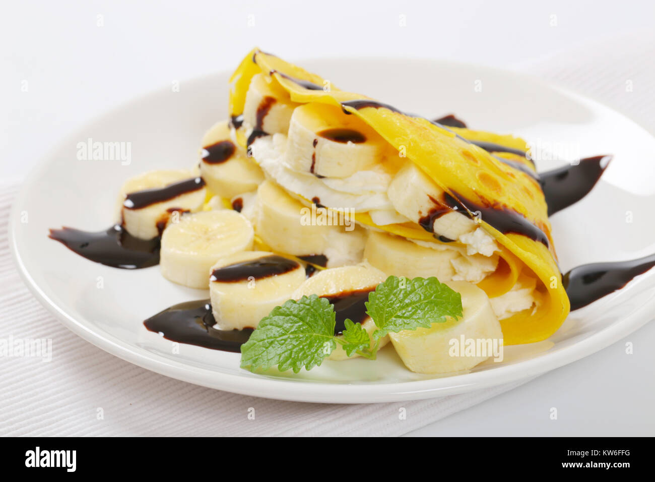 Crepes mit Bananenscheiben, Schlagsahne und Schokoladensauce Stockfoto