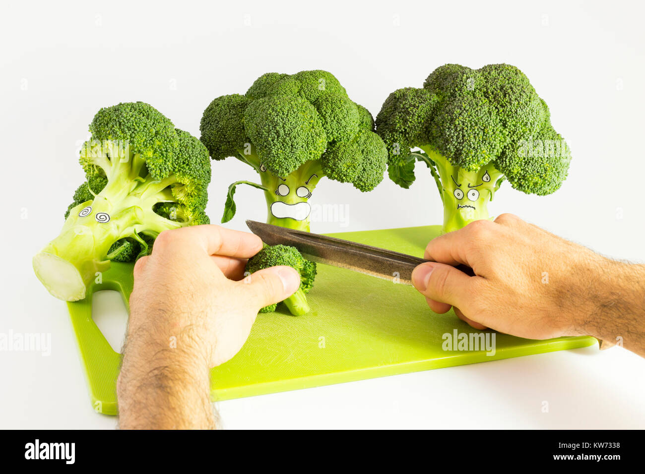 Nahaufnahme von zwei Händen schneiden frisches Grün Brokkoli mit Angst Cartoon Stil Flächen auf einem grünen Kunststoff Schneidbrett mit einem Vintage Küchen Messer mit r Stockfoto