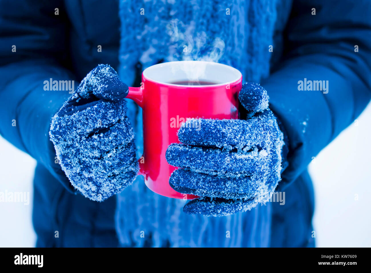 Weibliche Hände in Handschuhe halten roten Tasse mit Dampfenden dunklen Drink auf Winter Tag Stockfoto