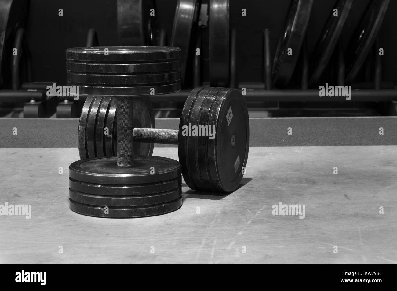 Schwarz-weiß Bild von zwei alte und gebrauchte schwarze Kurzhanteln auf einem Holzboden in ein Fitnessstudio. Stockfoto