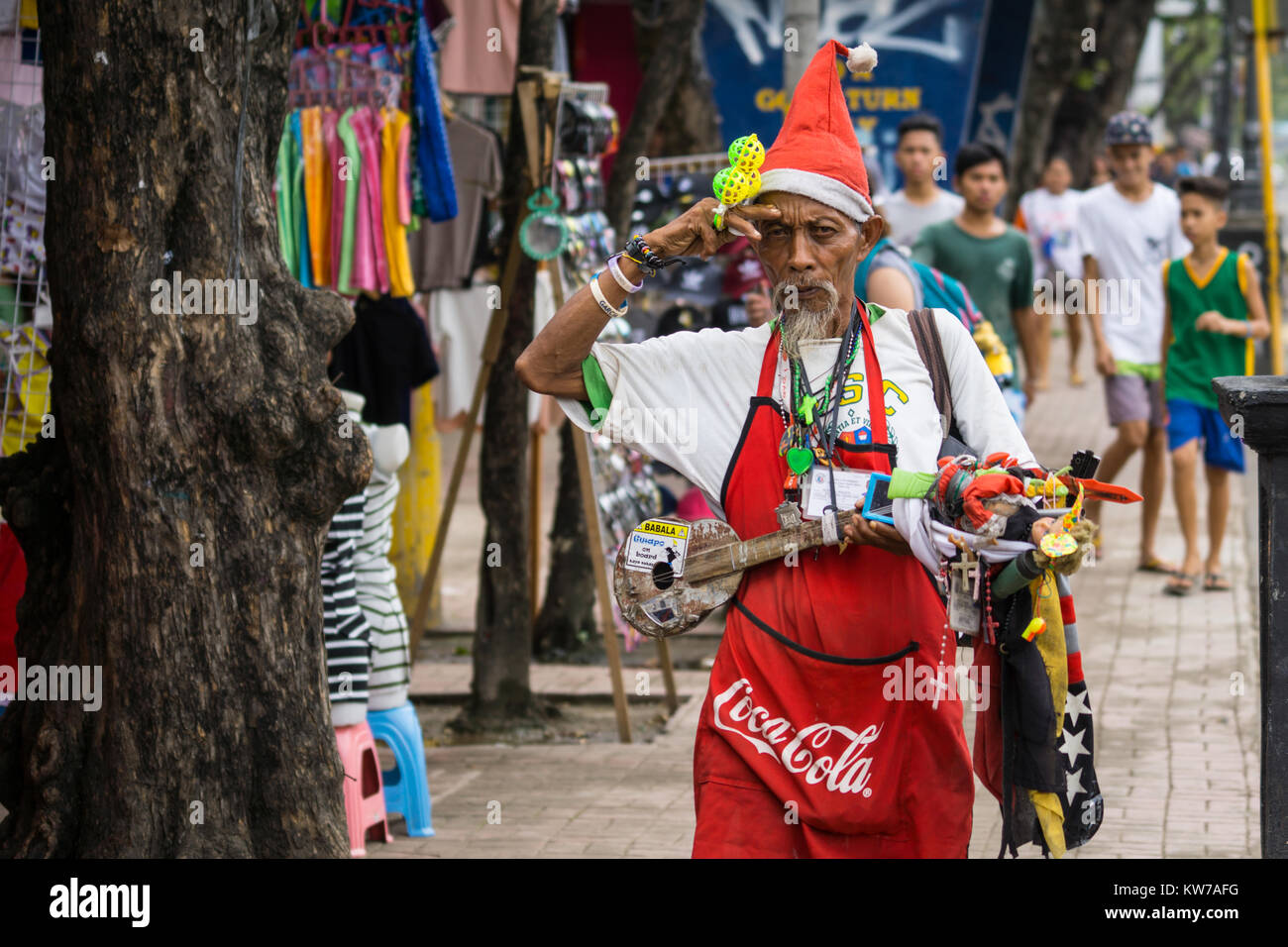 Filipino Mann im Santa Hut, Coca Cola Schürze & Musical Instrument, wie er singt Weihnachtslieder um Cebu City, Philippinen Stockfoto