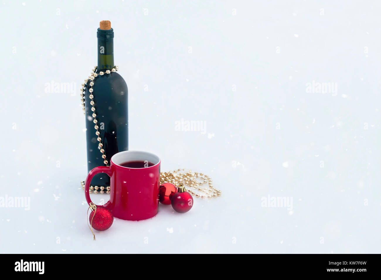 Flasche Wein mit roten Tasse und Weihnachtsschmuck auf Schnee mit Schnee vom Himmel Stockfoto