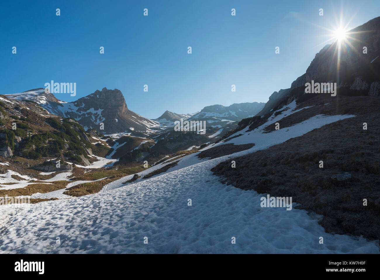 Sonne mit Sonnenstrahlen in den wolkenlosen Himmel über einem Schneefeld unterhalb der Gipfel der Rofangebirge im Frühjahr, Tirol, Österreich Stockfoto