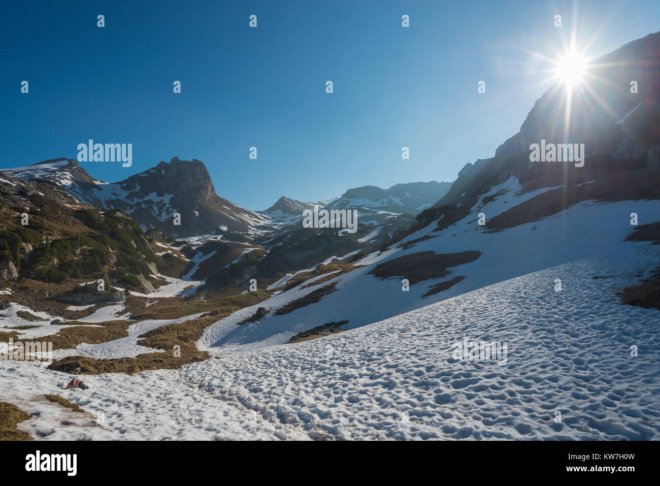 Sonne mit Sonnenstrahlen in den wolkenlosen Himmel über einem Schneefeld unterhalb der Gipfel der Rofangebirge im Frühjahr, Tirol, Österreich Stockfoto