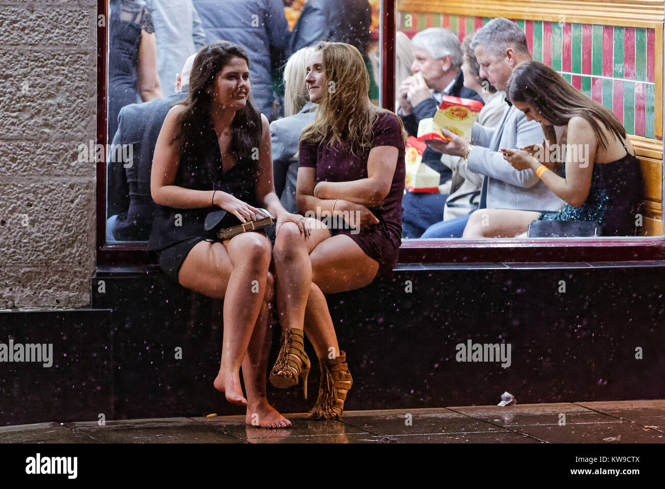 Zwei junge Frauen, von denen eine ist barfuß, auf den Fenstersims eines Takeaway rest Stockfoto