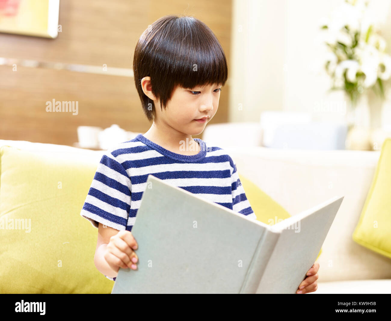 8 Jahre alten kleinen asiatischen Jungen Sofa ein Buch zu Hause lesen. Stockfoto