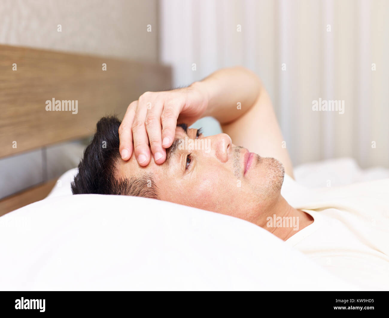Asiatischer Mann liegend auf Bett Augen mit der offenen Hand auf die Stirn gedrückt, müde oder frustriert. Stockfoto