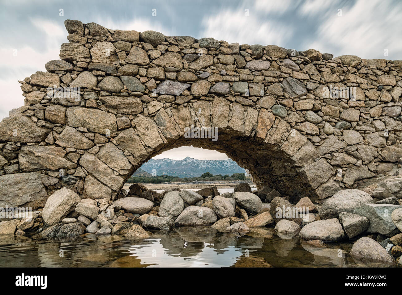 Blick auf schneebedeckte Berge durch den Bogen von einer kleinen Steinbrücke am Lac de Codole in der Balagne Korsika Stockfoto