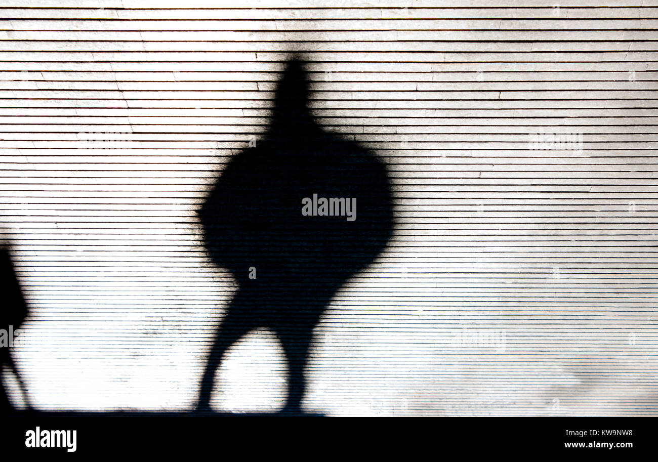 Blurry krumme Schatten Silhouette einer Person zu Fuß Straße der Stadt gemusterten Bürgersteig in Schwarz und Weiß Stockfoto