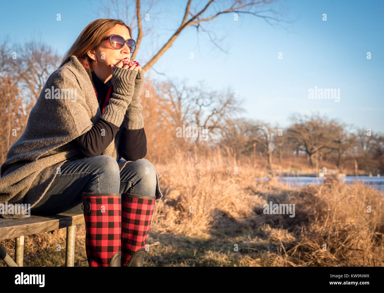 Frau sitzt am See im Winter beobachten, Sonnenuntergang in Pullover und Strick Handschuhe Stockfoto