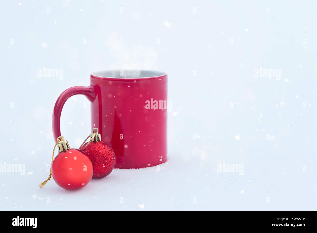 Rot Tasse mit heißem Getränk auf Schnee mit zwei roten Kugeln mit Schnee im Winter Tag Stockfoto
