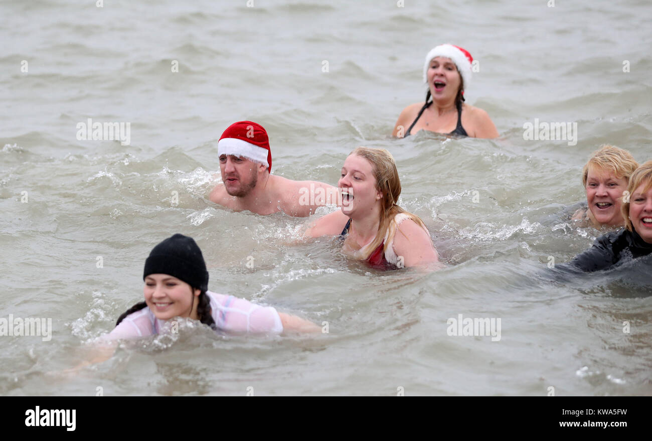 Kris Smith, 24, (Zweite links) und Jade Slater, 21, (Mitte), um den Solent, wie sie in der Gosport und Fareham küstennahe Rettungsdienst jährlichen Tag des Neuen Jahres Schwimmen in Gosport, Hampshire. Stockfoto