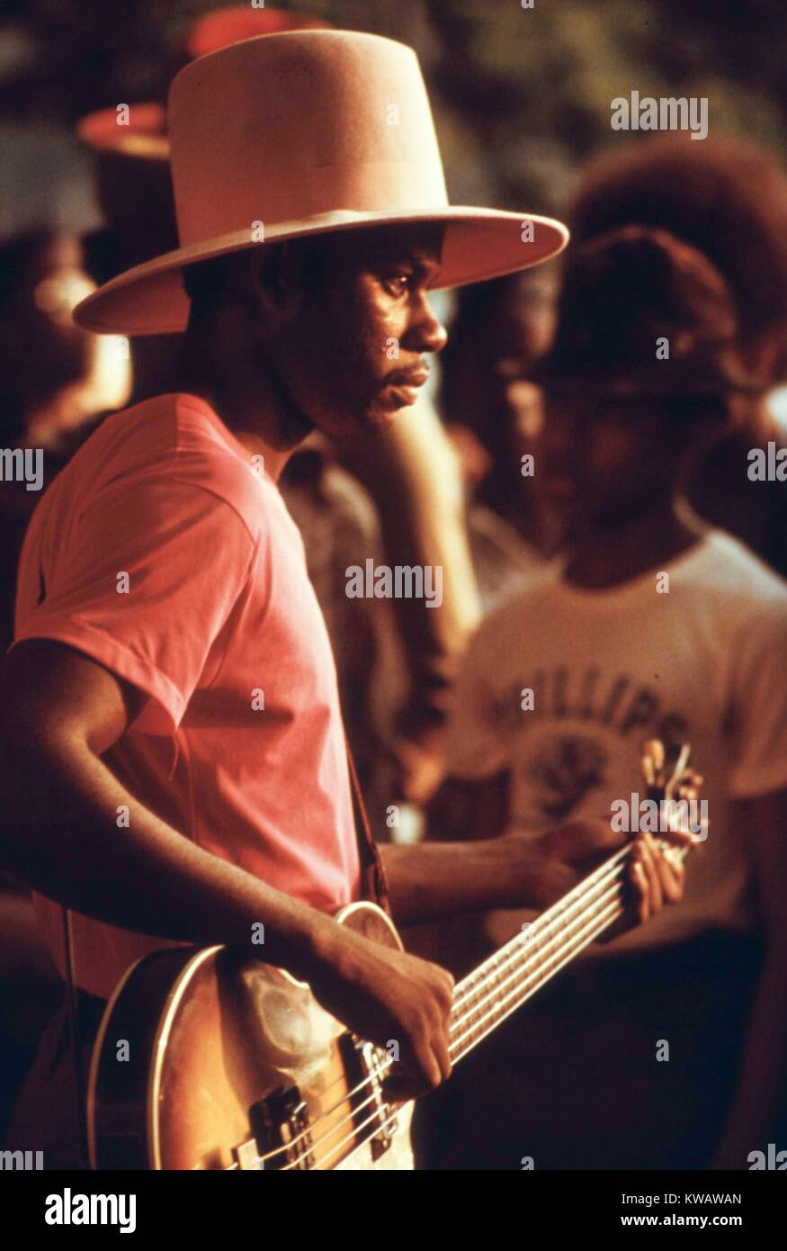 Ein junger Gitarrist mit rosa T-Shirt und Top hat Strums einige Melodien wie die Sonne außerhalb Lake Village Shopping Center in Chicago, Illinois, 1973. Mit freundlicher Genehmigung der nationalen Archive. Stockfoto