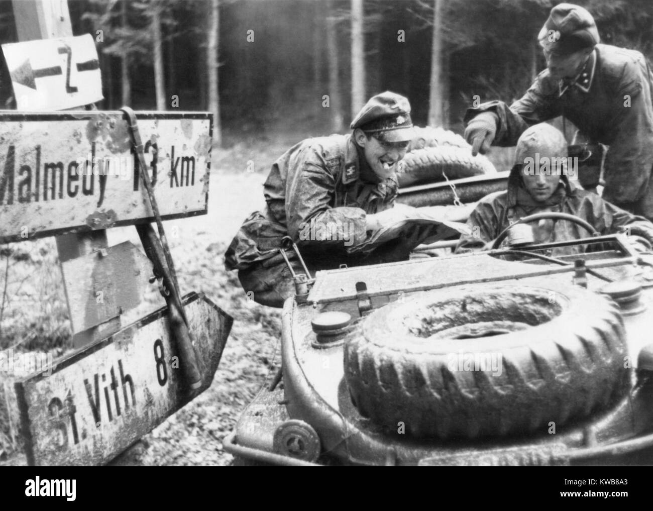 Deutsche SS-Truppen mit der 1. Panzerdivision prüfen ein Hinweisschild an einer Kreuzung der Ardennen. Ein Ziel auf dem Schild, Malmedy, wäre der Standort eines NS-Massaker an 84 unscharf amerikanischen Kriegsgefangenen in der Schlacht der Ausbuchtung geworden. Immer noch von einem erfassten deutschen Film. Ca. Dez. 10-17, 1944. Weltkrieg 2. (BSLOC 2014 10 91) Stockfoto