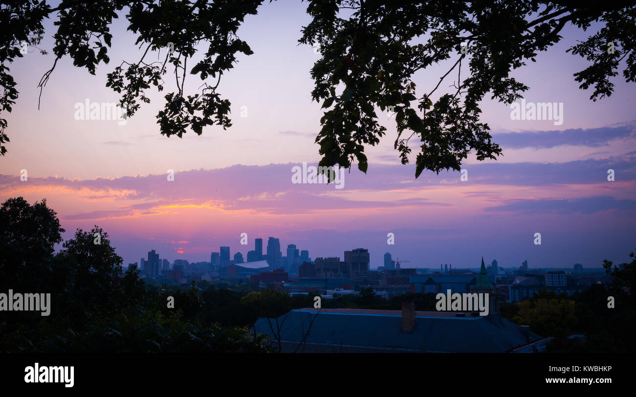Sonnenuntergang mit dem Minneapolis Minnesota Skyline mit Blättern und Zweigen gerahmt. Himmel ist Rosa, Blau, Orange und Violett mit niedrigen Horizont der Wolkenkratzer. Stockfoto