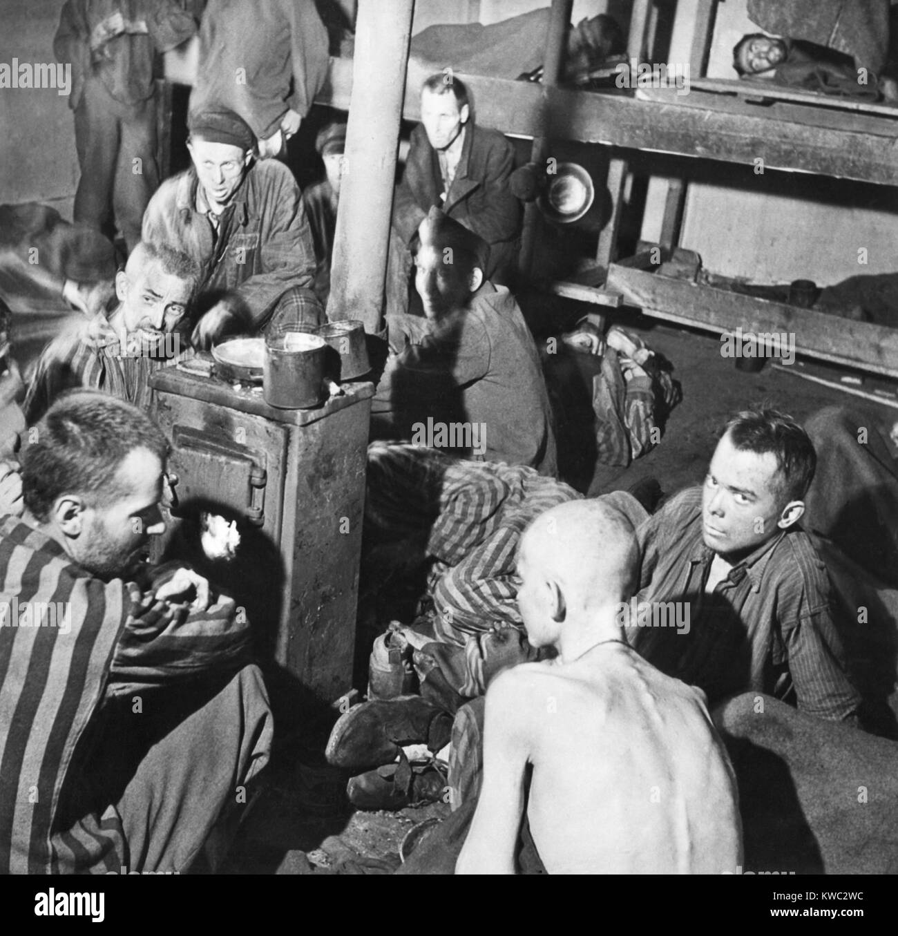 Sandbostel Gefangenenlager überlebenden Sitzen um einen Herd Feuer nach dem Britischen Befreiung, 30. April 1945. Sie waren unter 8000 zivilen und politischen Gefangenen getrennt untergebracht und behandelt werden viel schlimmer als 15.000 alliierte Militärs Gefangene. Der Mann auf dem Stock auf der Rückseite dieses Bildes ist tot, aber die anderen nicht bemerken. (BSLOC 2015 13 12) Stockfoto