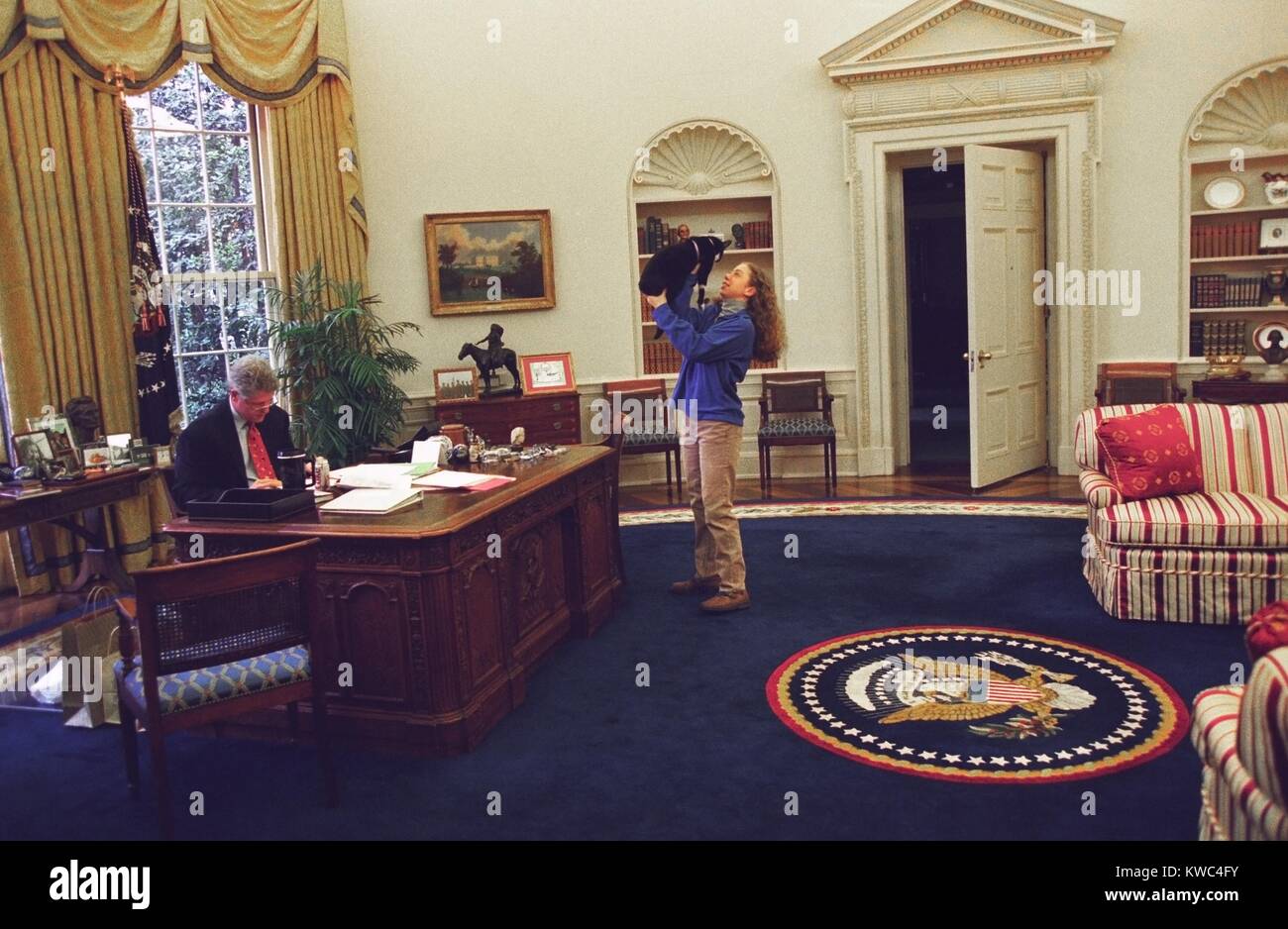 Chelsea Clinton die Katze im Oval Office mit Socken spielen. Auf der linken Seite, Präsident Bill Clinton arbeitet an seinem Schreibtisch. 24. Dezember 1994. (BSLOC 2015 2 201) Stockfoto