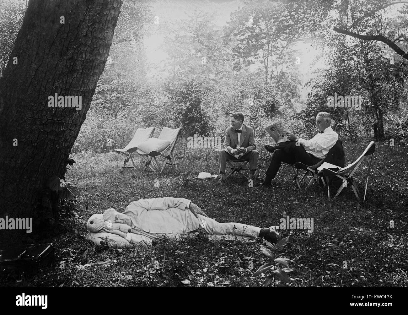 Thomas Edison nap unter einem Baum, am 19. Juli 1921. Im Hintergrund der Präsident Warren Harding liest eine Zeitung in einem Lager Stuhl neben Harvey Firestone. Maryland. (BSLOC 2015 15 33) Stockfoto