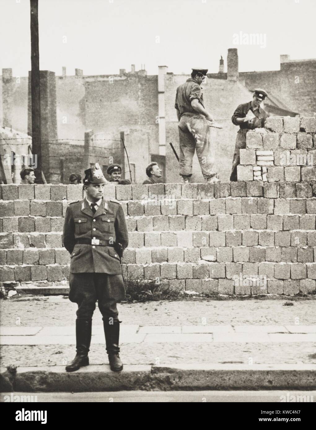 West-Berliner Polizist steht vor der Betonklotz Mauer zwischen Ost- und West-Berlin. Entlang der Bernauer Straße fügen Ost-Berliner Arbeiter Sie Blöcke, um die Höhe der Barriere zu erhöhen. 11. Oktober 1961. (BSLOC 2015 2 265) Stockfoto
