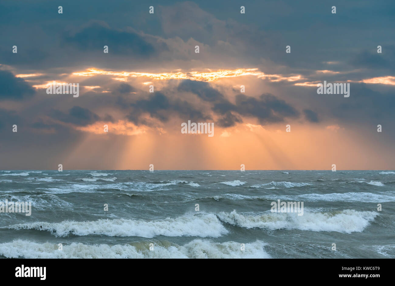 Niedrige Sonne durch die Wolken mit Sonnenstrahlen Übersicht über eine rauhe See im Winter in Großbritannien versteckt. Stockfoto