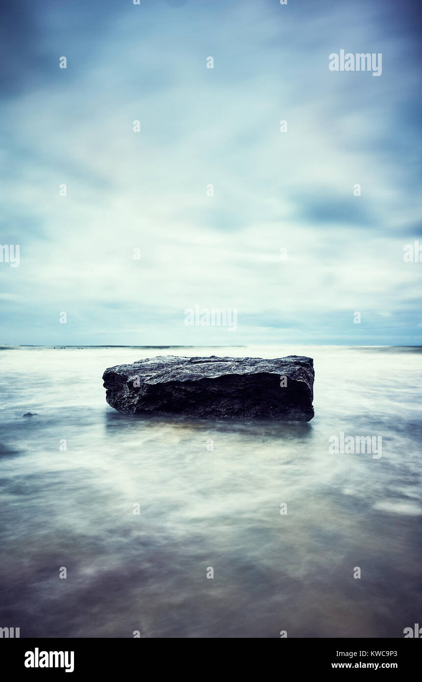 Stein am Strand, Bewegung verschwommen Wasser ruhige natürliche Hintergrund, Farbe getonte Bild, selektive konzentrieren. Stockfoto