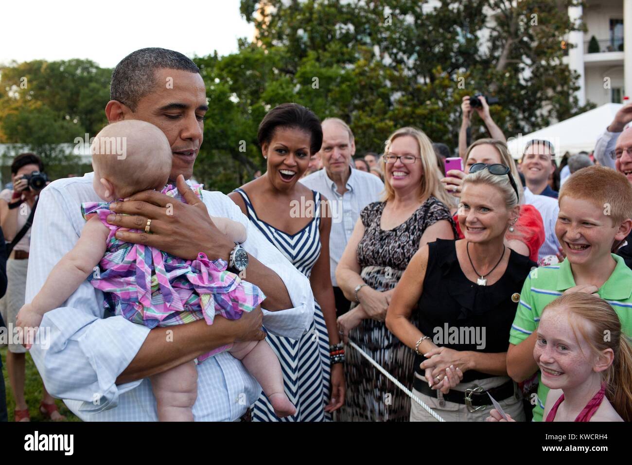Präsident Barack Obama beruhigt ein schreiendes Baby im Kongreß Picknick. Wenn er nahm das Baby von Michelle es hörte sofort auf zu schreien, damit Ihr und andere 'amüsiert Ausdrücke. South Lawn des Weißen Hauses, 15. Juni 2011. (BSLOC 2015 3 28) Stockfoto