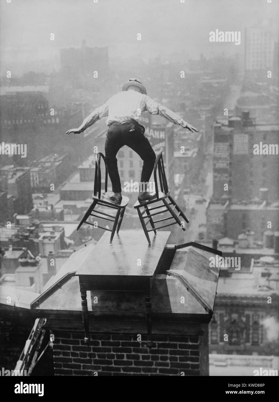 "Menschliche Fliegen 'John' Jammie "Reynolds Salden geneigt, der unsicher auf zwei Stühlen. Das dare-devil ist auf dem Dach von einem hohen Gebäude in Manhattan, auf eine Tabelle über einen Schornstein platziert thront. Ca. 1915-1920. (BSLOC 2015 17 170) Stockfoto