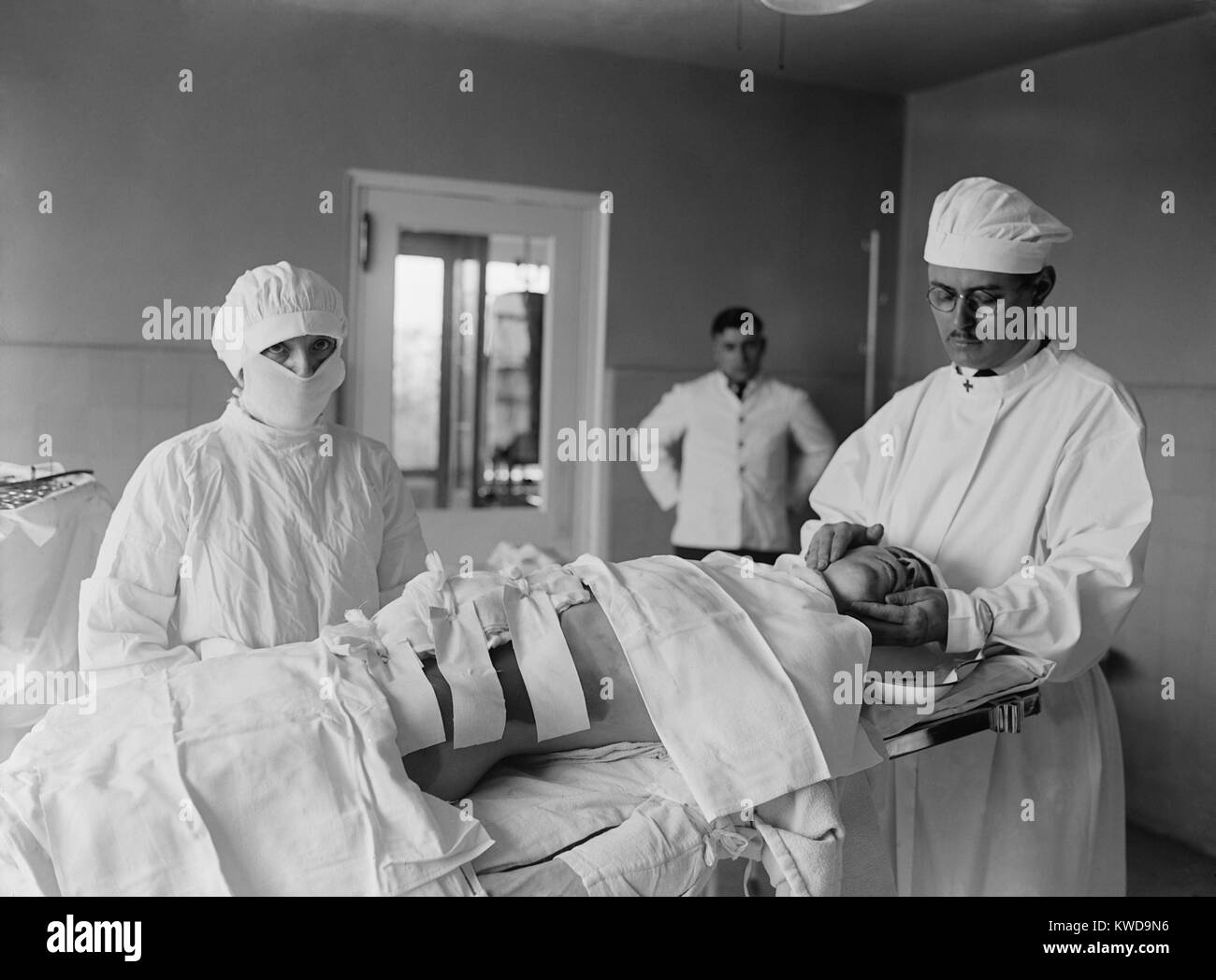 Anästhesist und OP-Schwester mit einer post-operativen Patienten. Eine große Bandage deckt den Schnitt, und die Haut wird von antiseptischen Lösung gefärbt. 1922 in einem Krankenhaus in Washington, D.C. (BSLOC 2016 10 37) Stockfoto