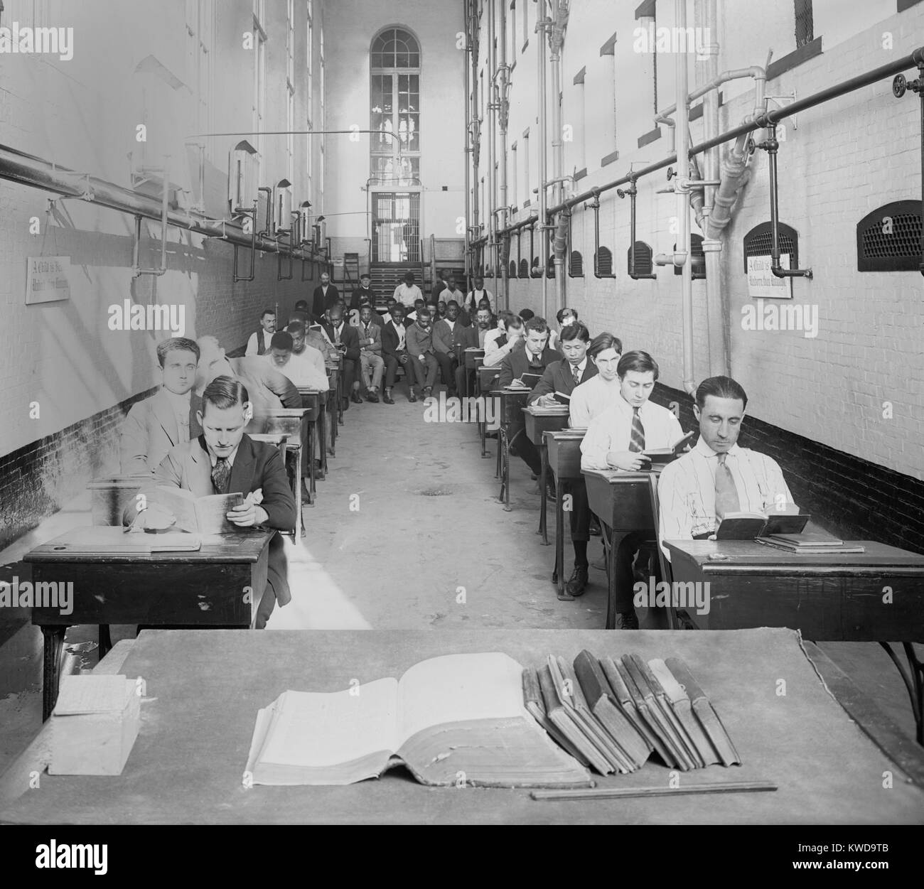 Junge Männer am Schreibtisch in einem amerikanischen Gefängnis C. 1920. Ein Zeichen liest, "ein Kind ist besser Ungeborenen als Nicht-belehrten." Die rassisch integrierten Gruppe sind gekleidet in ordentliche und saubere Hemden, Krawatten und Pullover (BSLOC 2016 10 72) Stockfoto