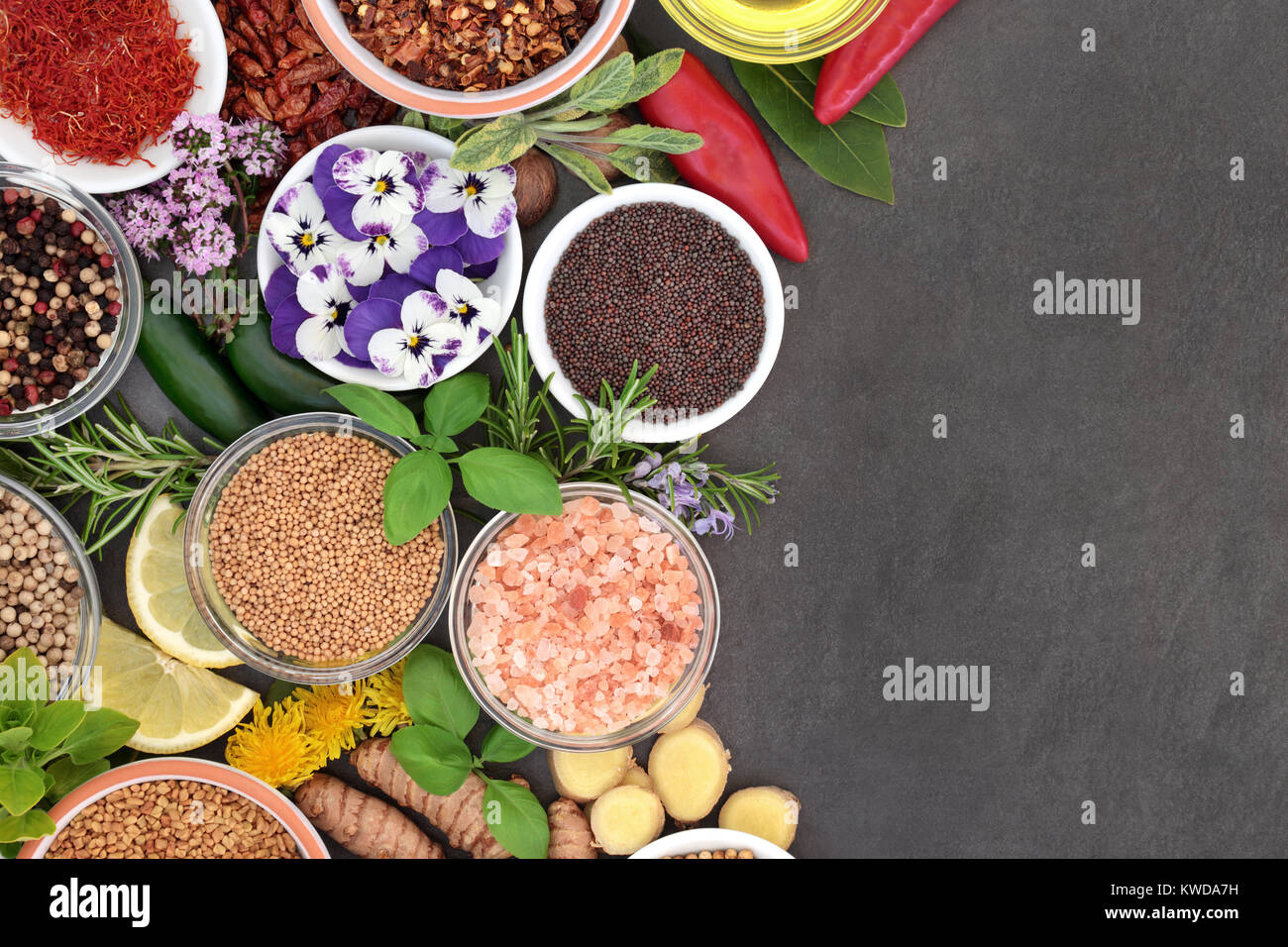 Gewürze, Kräuter und essbare Blüten bilden eine Zusammenfassung Hintergrund Grenze auf Schiefer. Stockfoto