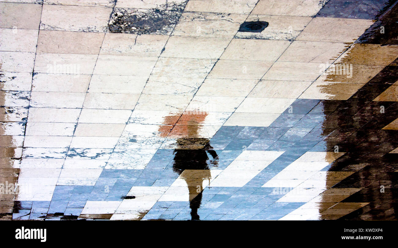 Reflexion Schatten Silhouette eines Mannes unter roten Regenschirm zu Fuß in die Altstadt gemusterten Platz im Regen Stockfoto