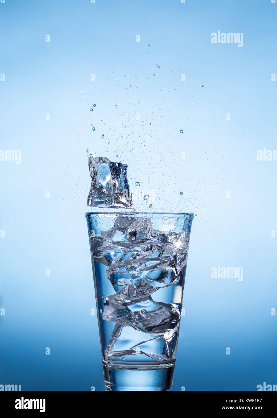 Spritzwasser Glas mit Eiswürfeln auf blauem Hintergrund, Nahaufnahme, Ansicht von vorne. Stockfoto
