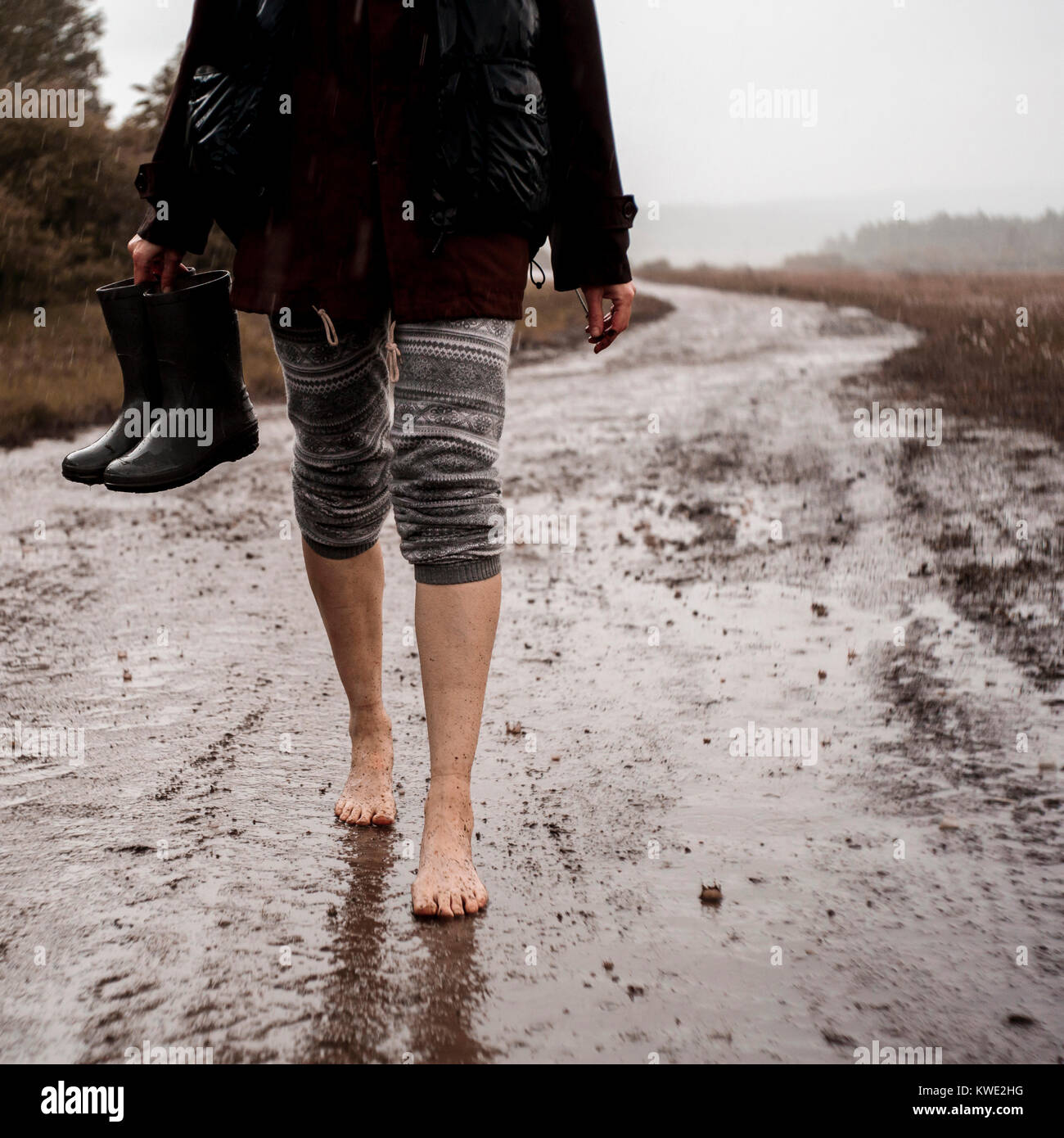 Untere Partie der Frau mit Gummistiefel beim Gehen auf nasser Piste Stockfoto