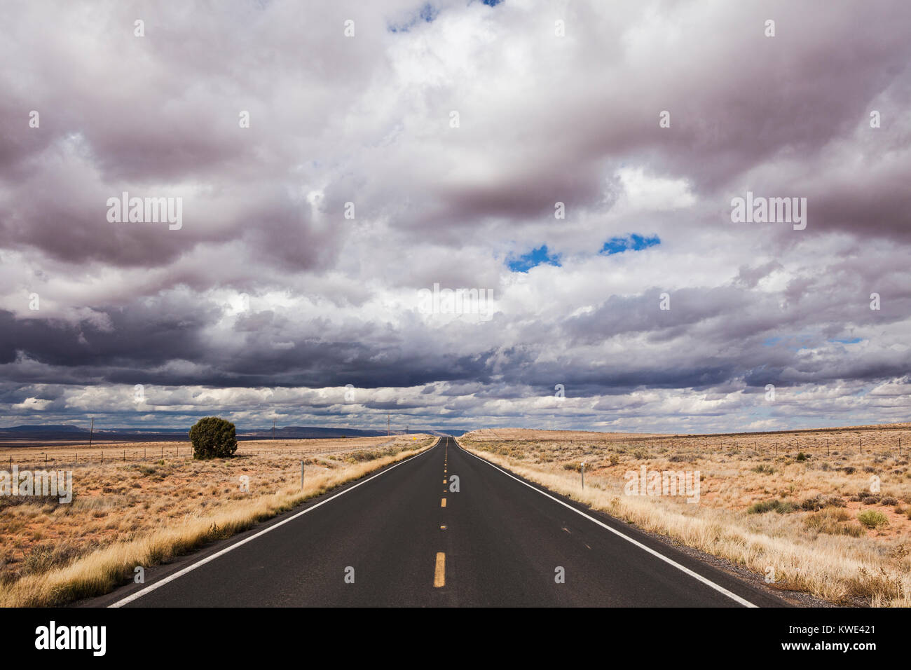 Leere Straße inmitten von Feld gegen stürmische Wolken Stockfoto