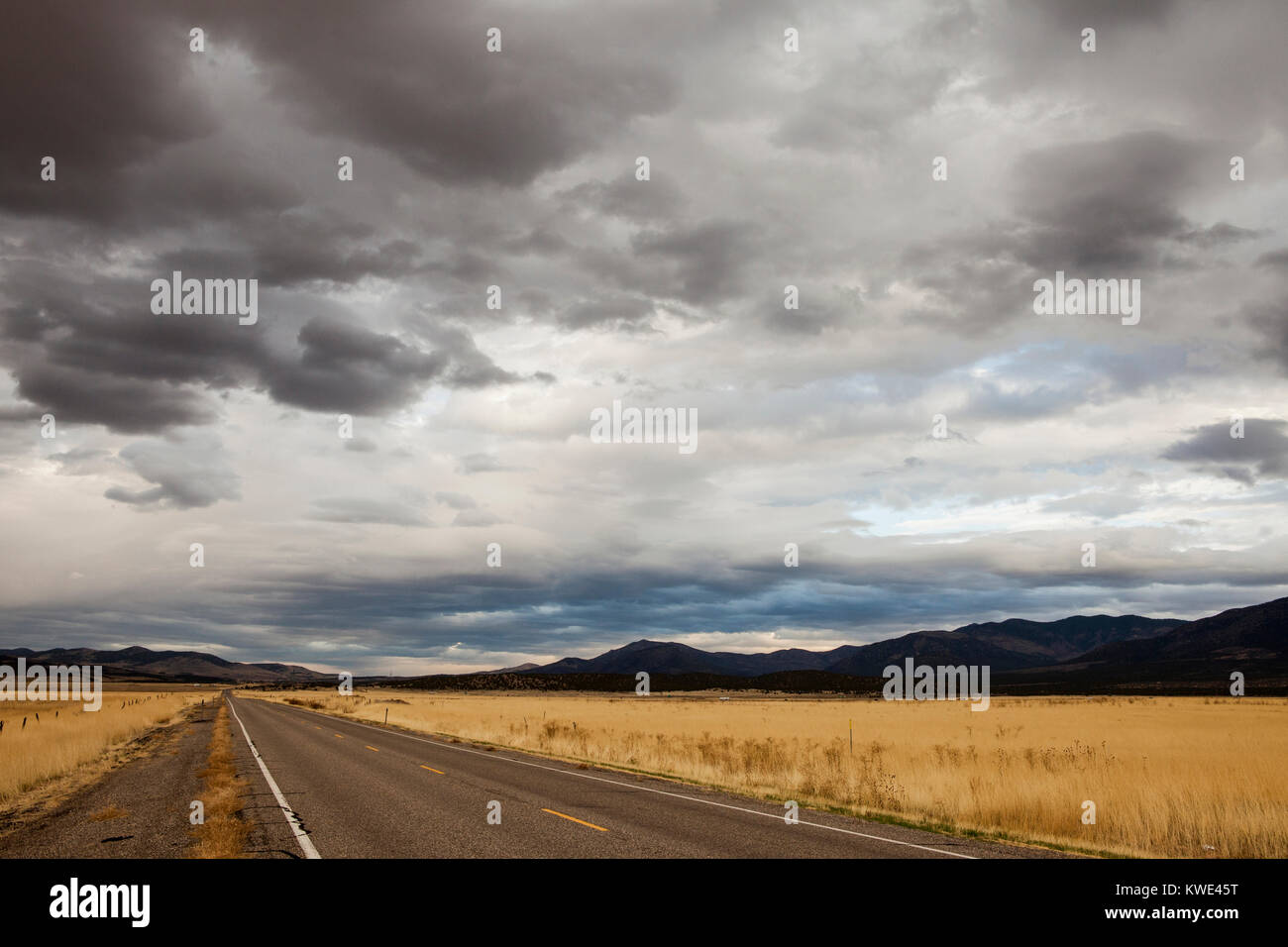 Country Road inmitten von Feld gegen stürmische Wolken und Berge Stockfoto