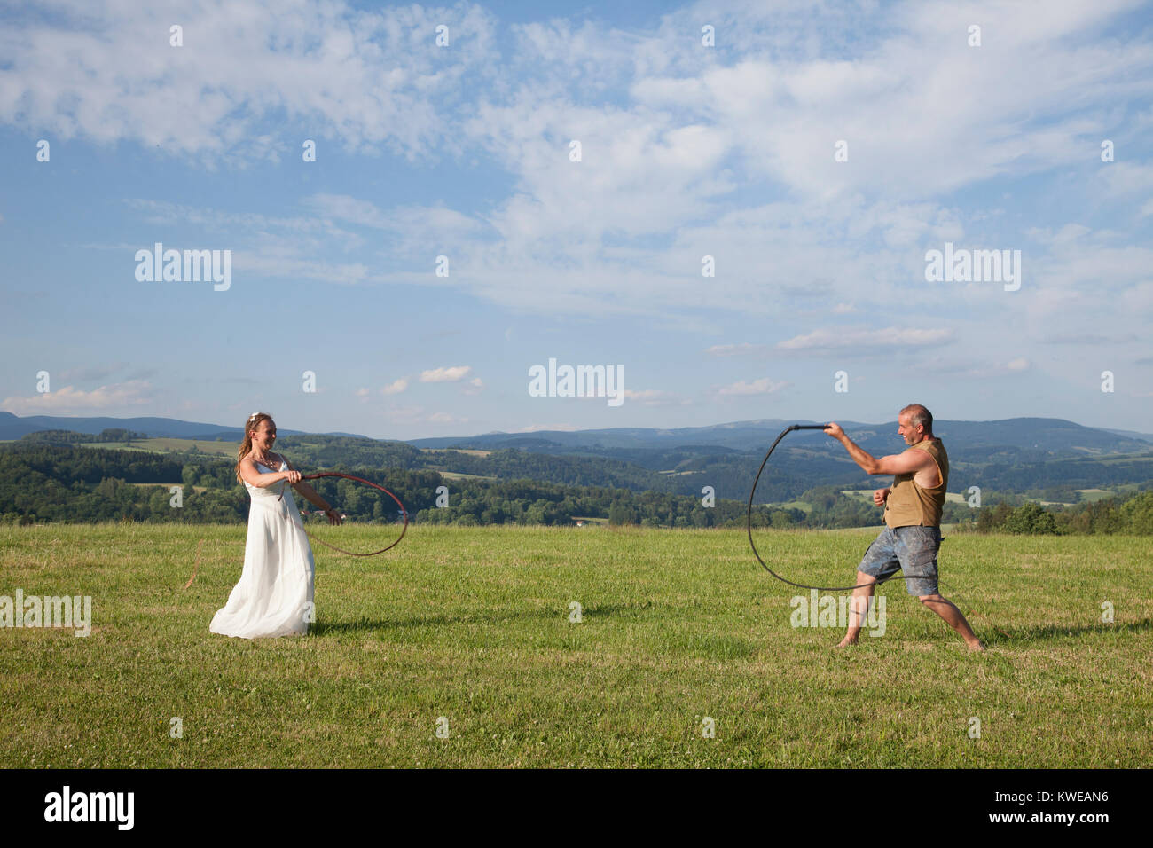 Der Mann und die Frau mit Hochzeit Kleid am Hochzeitstag in der Ausbildung ein Pferd Peitsche auf die grüne Wiese Wiese über Betrachtung großen Landschaft im Sommer. Stockfoto